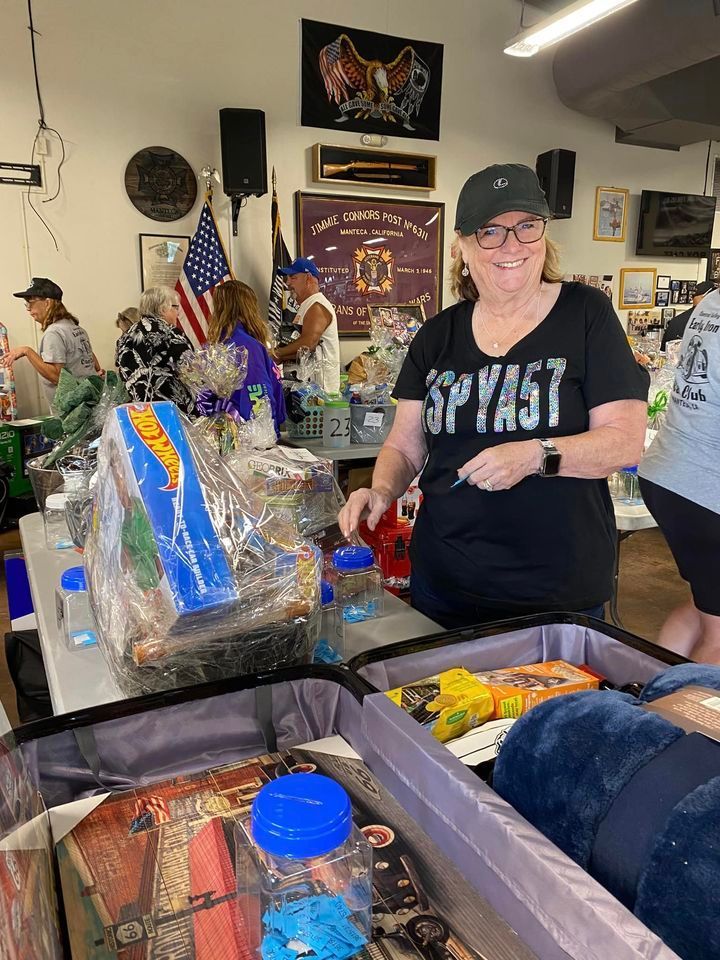 A woman wearing a spyast shirt is standing in a room filled with luggage.