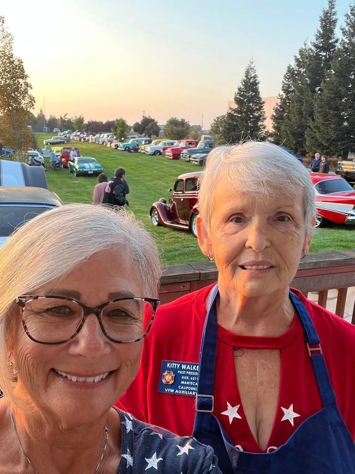 Two older women are posing for a picture at a car show.