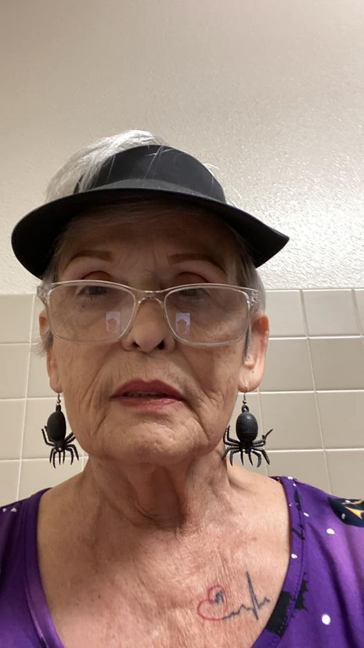 An elderly woman wearing a hat , glasses and spider earrings.