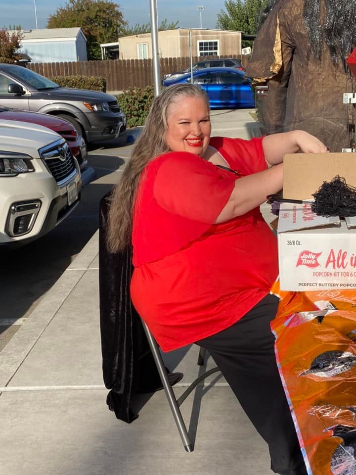 A woman in a red shirt is sitting at a table in a parking lot.