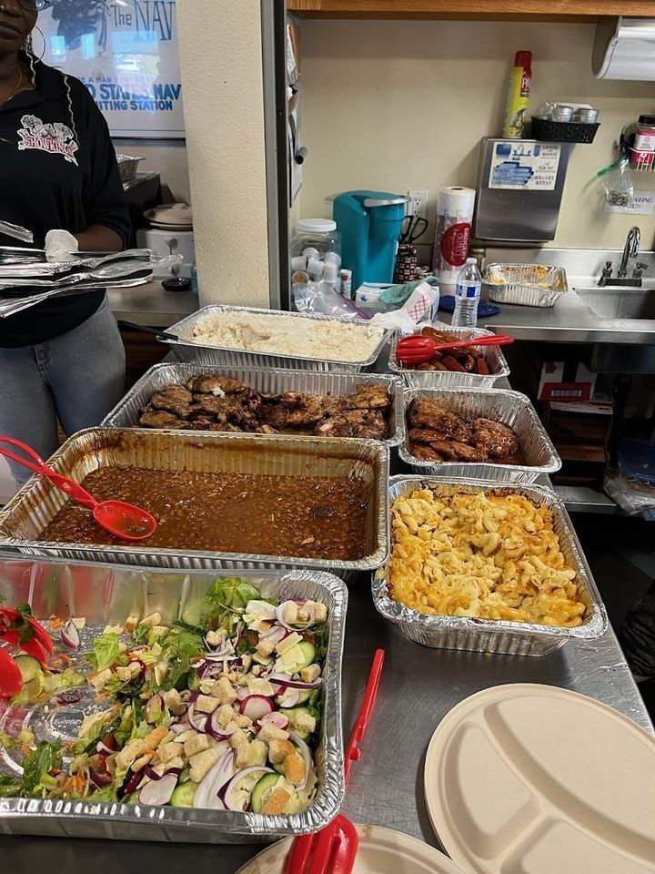 A woman is standing in front of a table filled with trays of food.