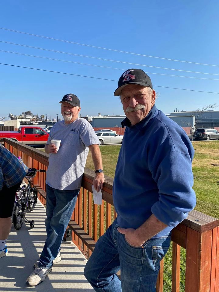 Two men are leaning on a railing on a deck.