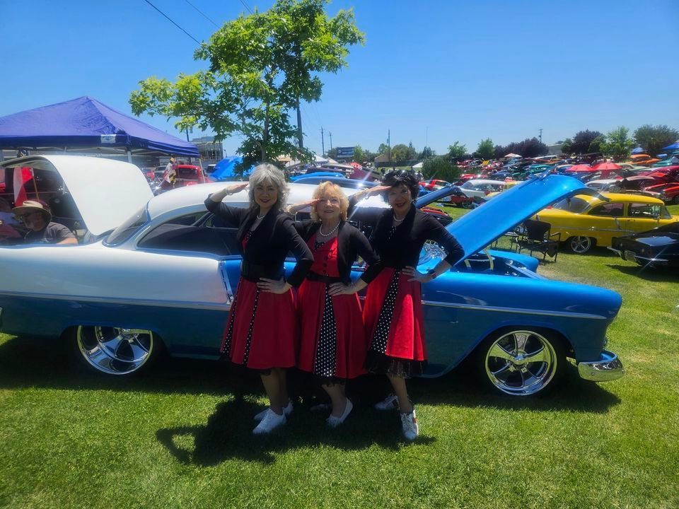 Three women are posing in front of a blue and white car