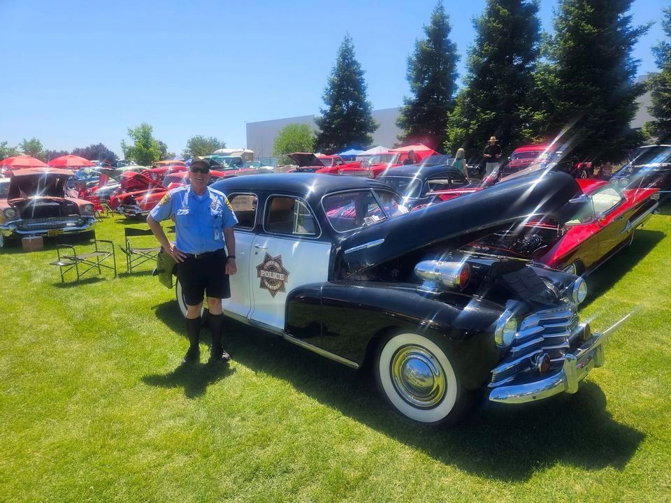 A man in a police uniform stands next to an old police car