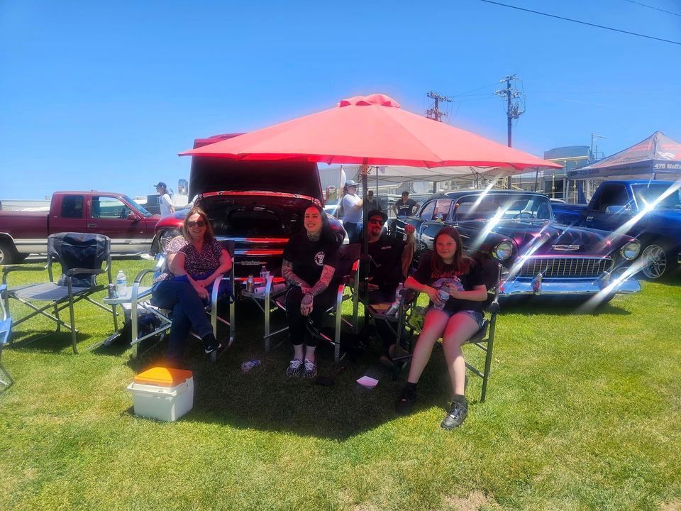 A group of people are sitting under a red umbrella in a field.