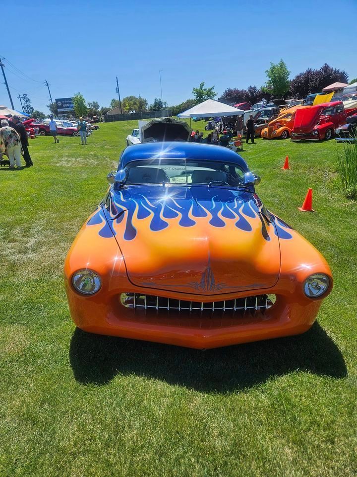 An orange car with blue flames painted on it is parked in a grassy field.