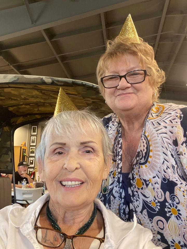 Two older women wearing party hats and glasses are posing for a picture.