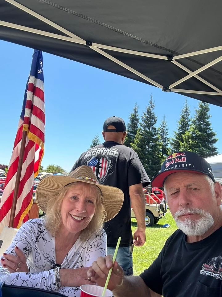 A man and a woman are sitting under a tent with an american flag in the background.