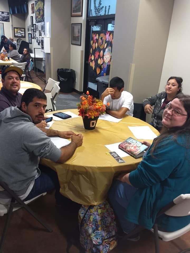 A group of people are sitting around a table with a vase of flowers on it.