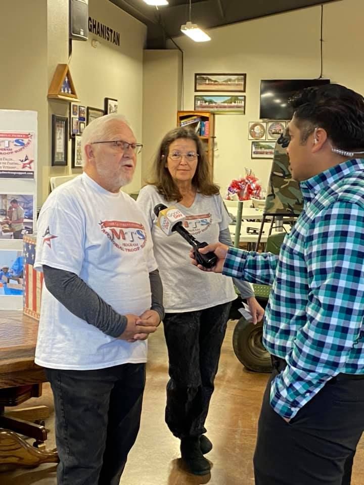 A man is holding a microphone while talking to two people in a room.