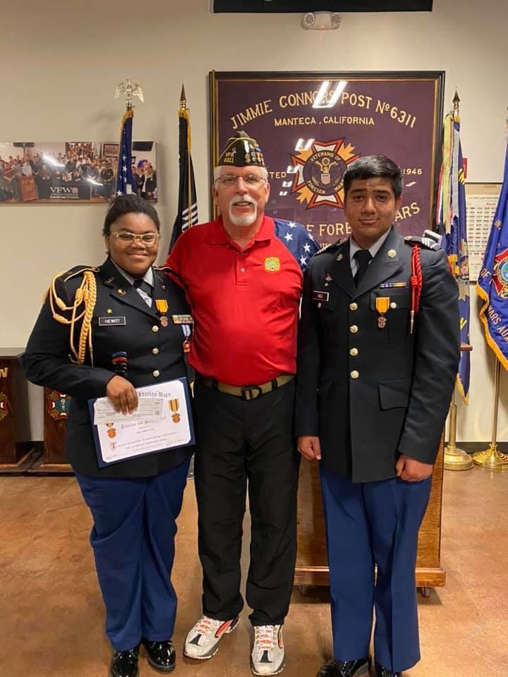 Three people in military uniforms are posing for a picture with a man in a red shirt.