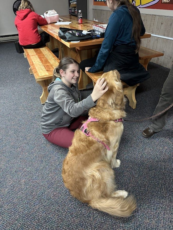 A girl is petting a dog while sitting at a picnic table.