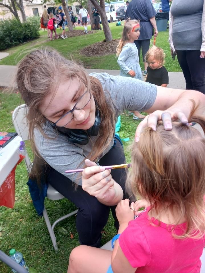 A woman is painting a little girl 's face in a park.