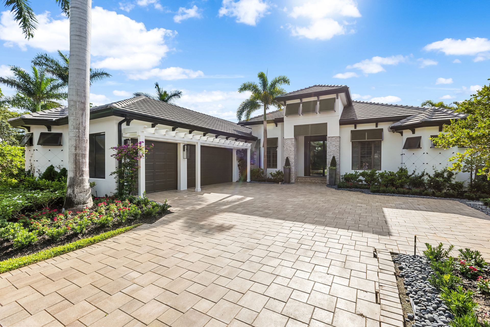 A Large White House with A Brick Driveway and Palm Trees in Front of It.