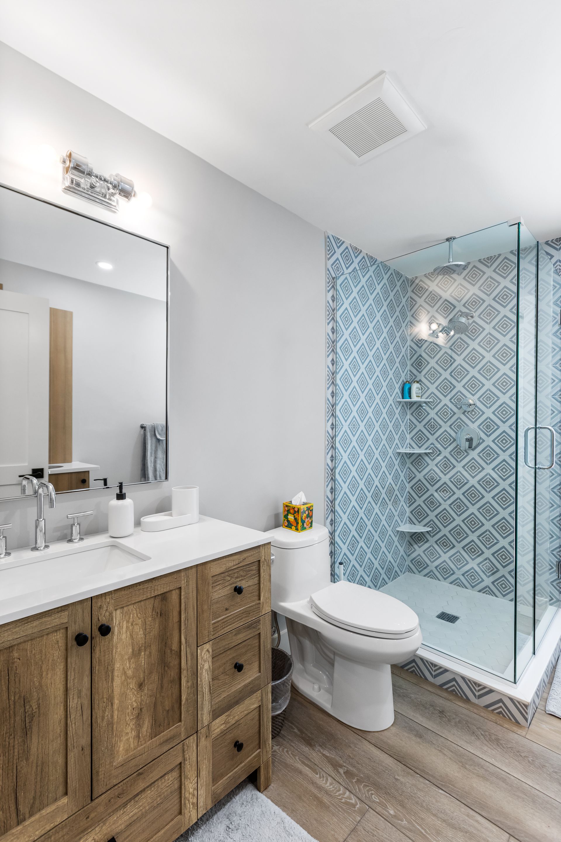 A bathroom with a toilet , sink , mirror and walk in shower.