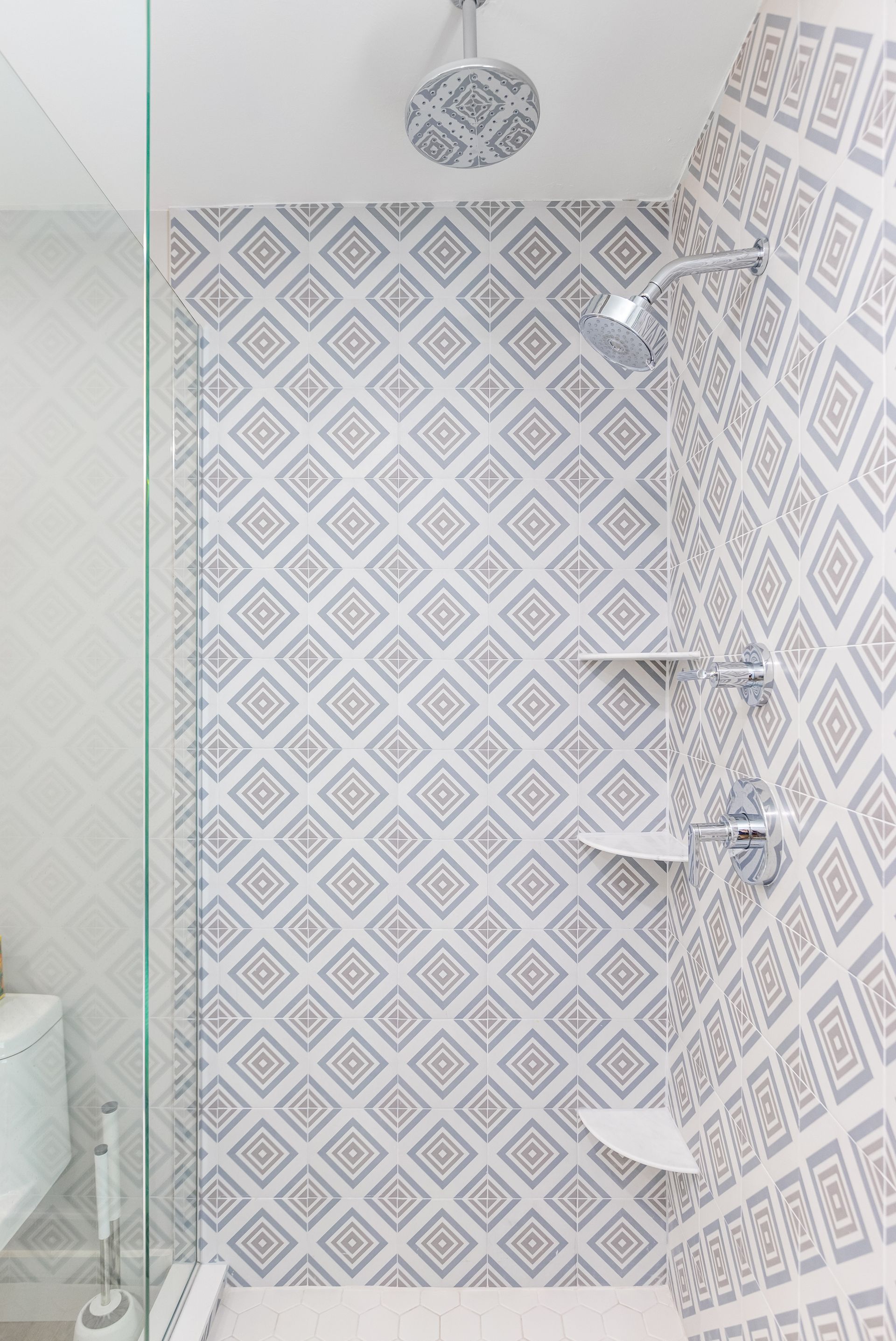 A bathroom with a walk in shower with a geometric pattern on the wall.