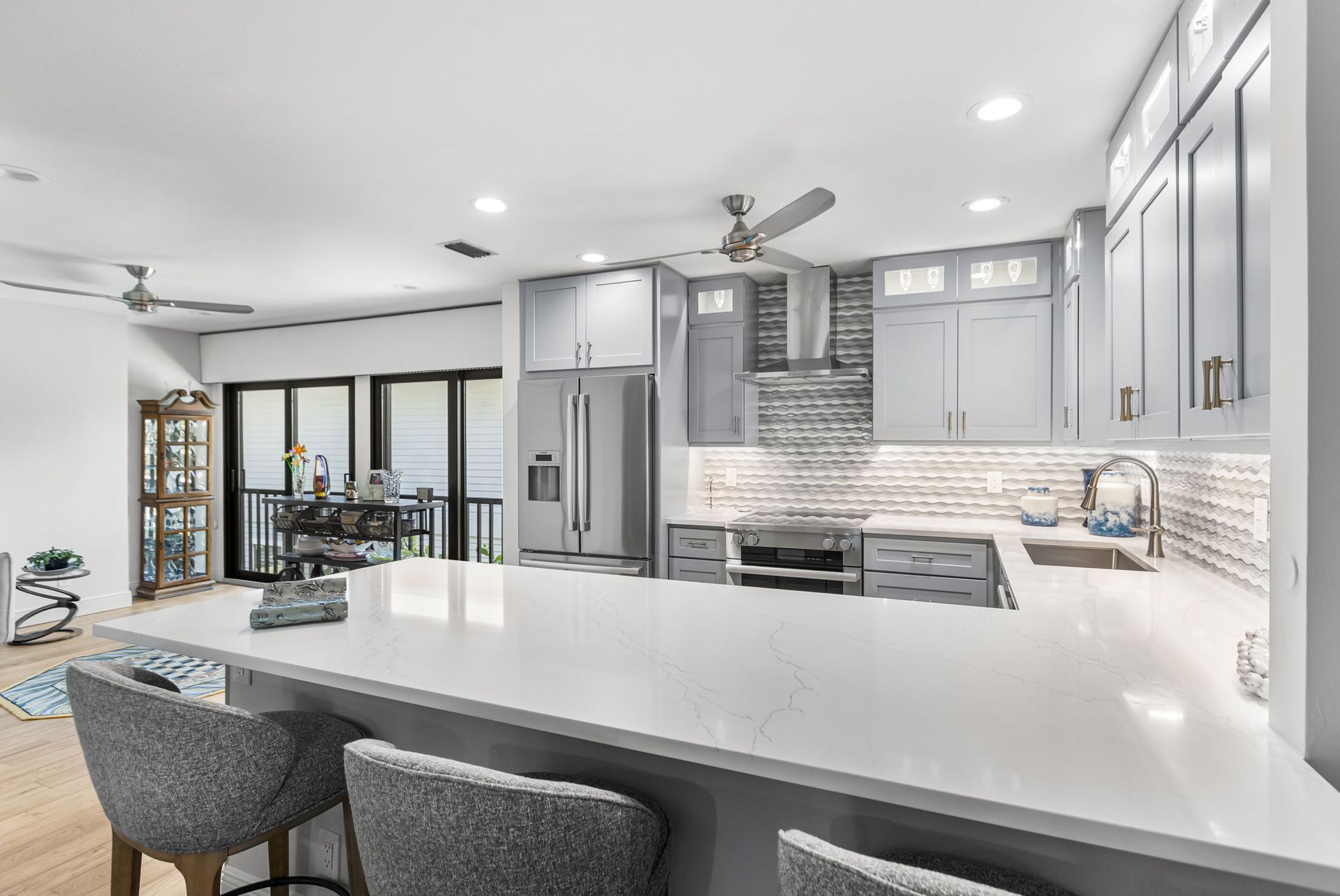 A kitchen with gray cabinets , white counter tops , stainless steel appliances and a ceiling fan.