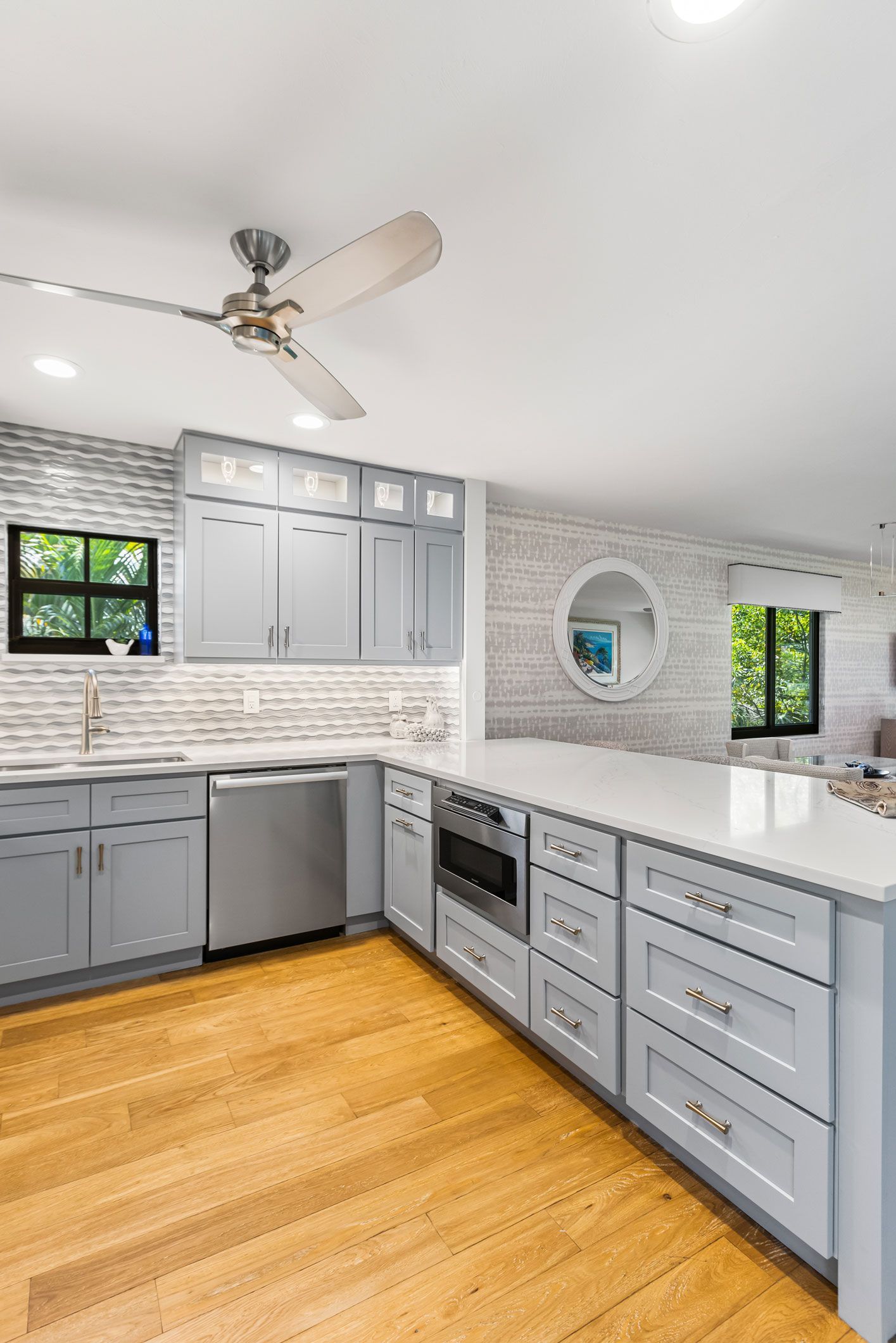 A kitchen with gray cabinets , white counter tops , and a ceiling fan.
