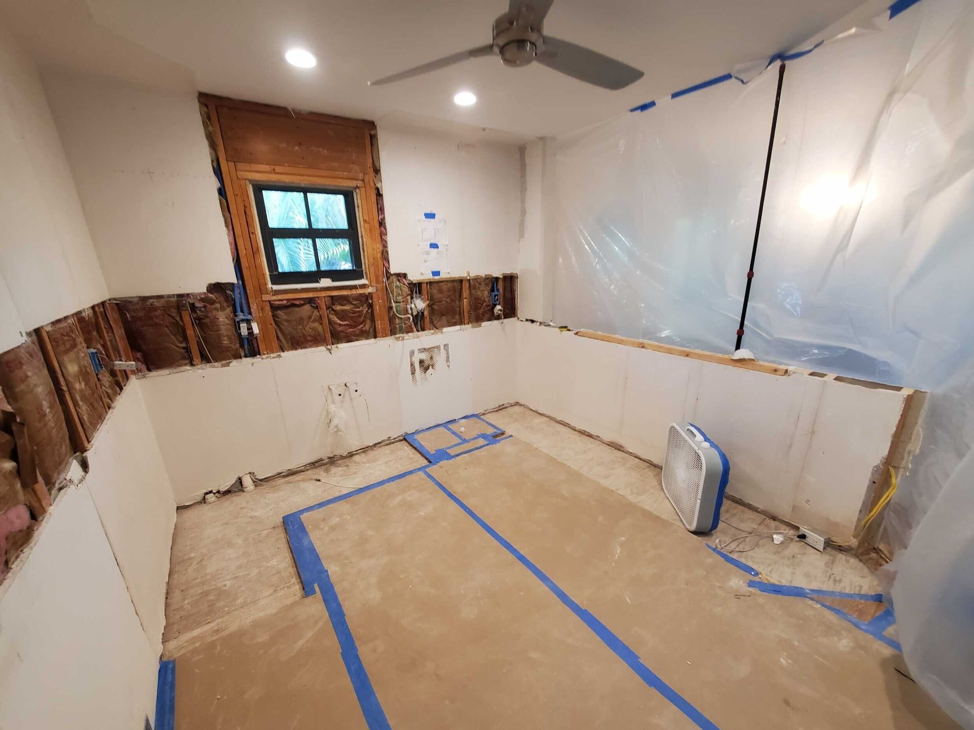A bathroom under construction with a ceiling fan and a window.