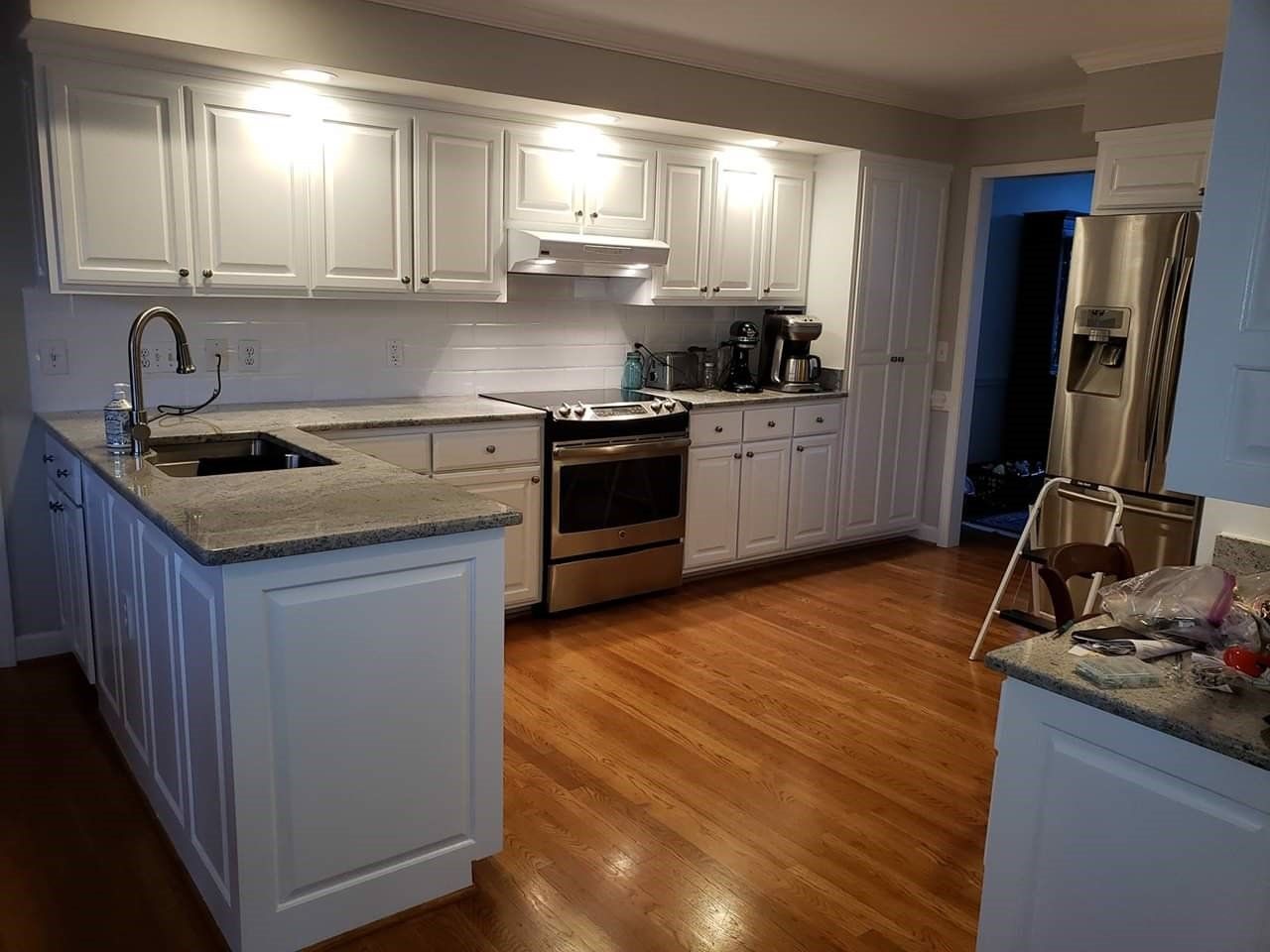 a kitchen with white cabinets , granite counter tops , stainless steel appliances and hardwood floors .