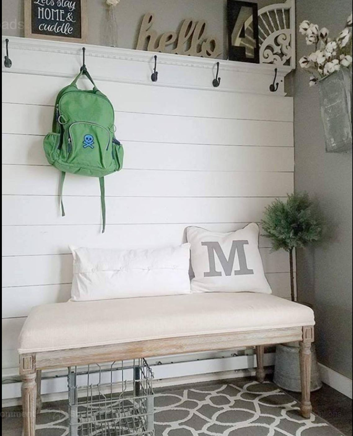 a green backpack is hanging on a hook above a bench in a hallway .