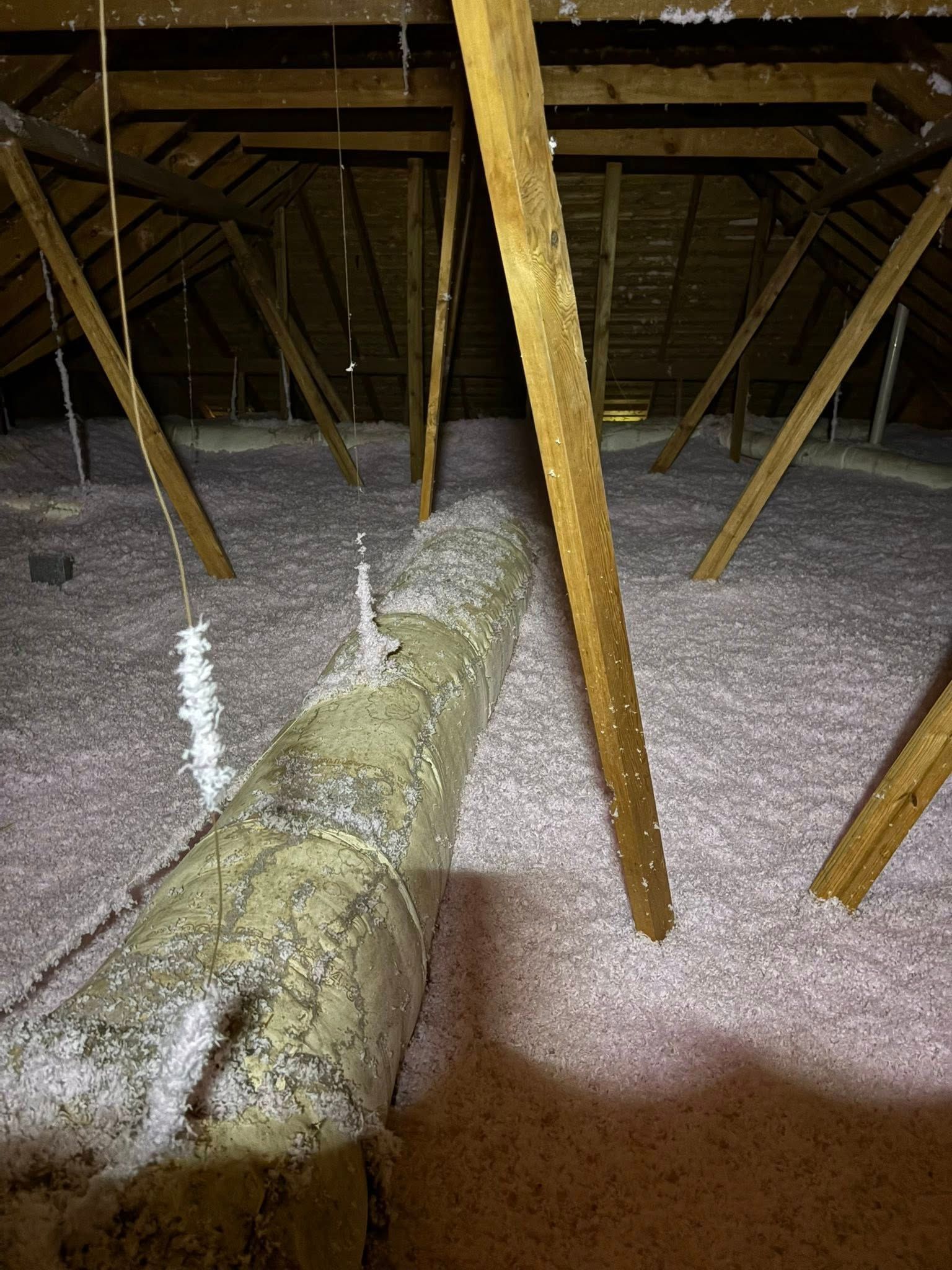 Attic with exposed rafters, insulation, and a large duct running across the floor
