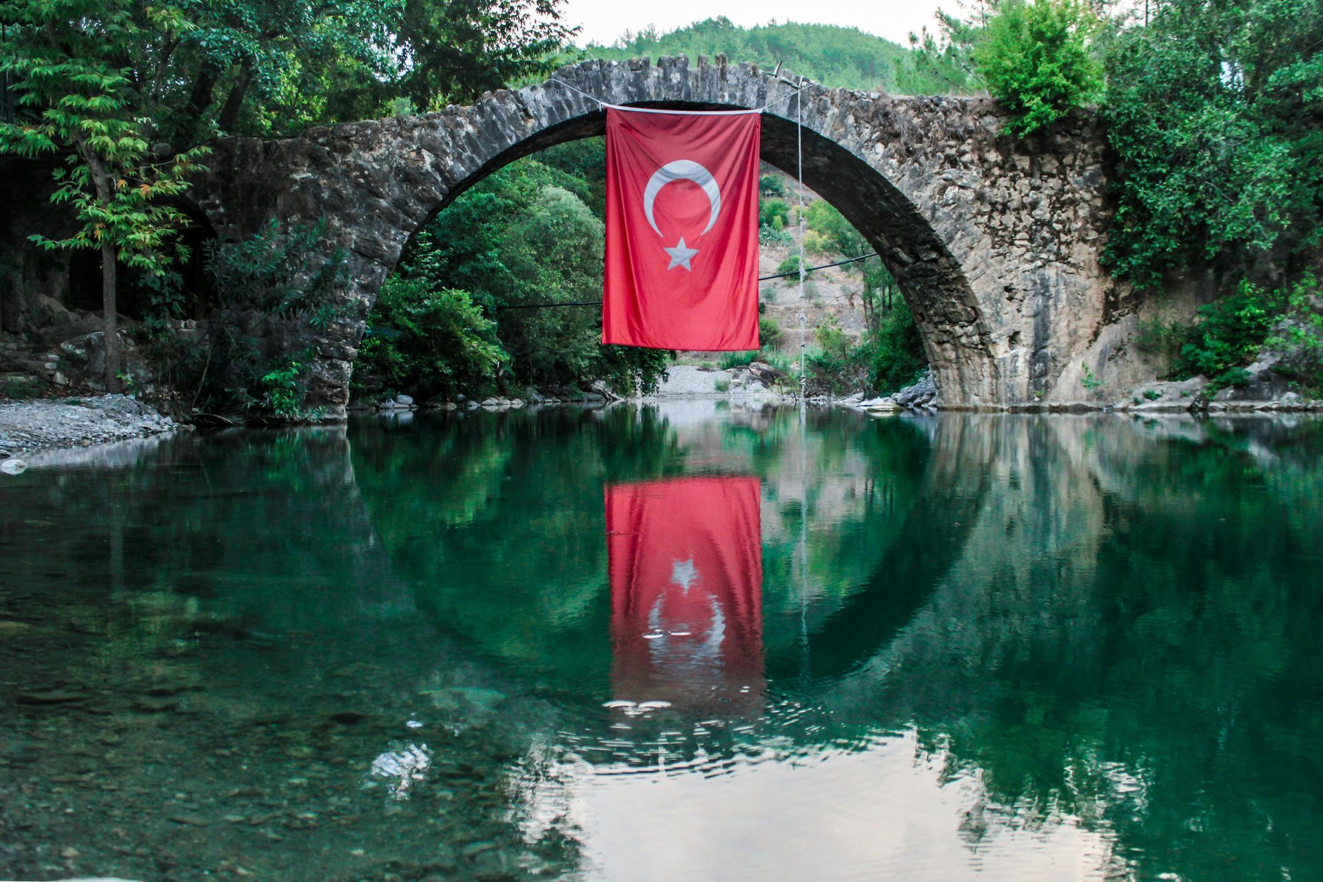 A red flag is hanging from a stone bridge over a river.
