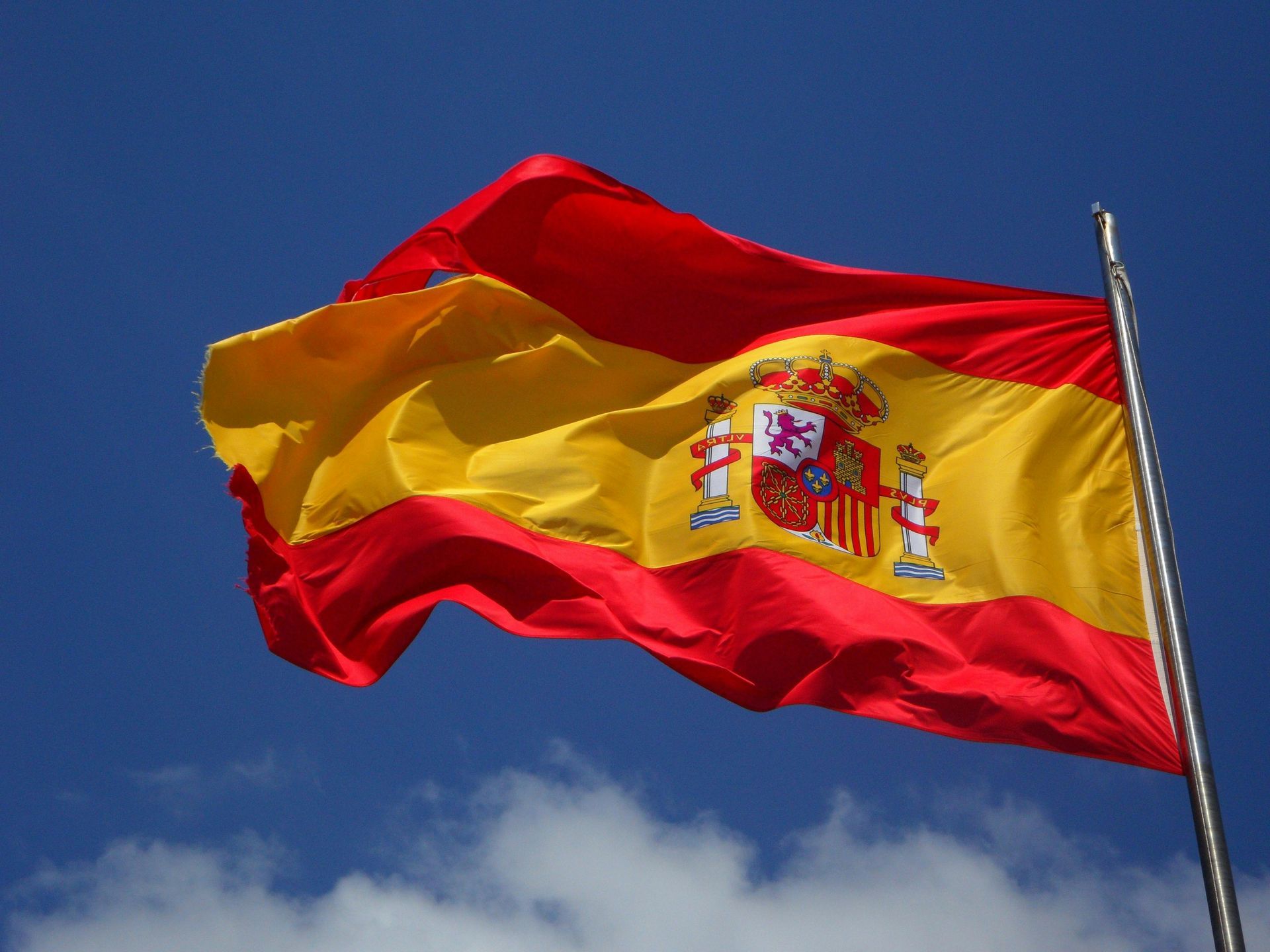 A spanish flag is waving in the wind against a blue sky