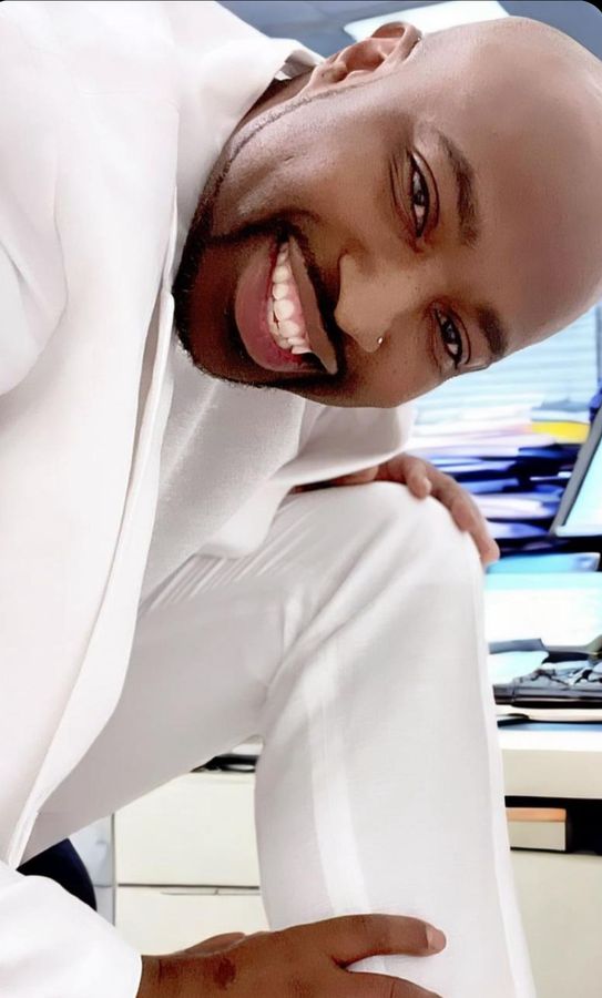 A bald man with a beard is wearing a white suit and smiling