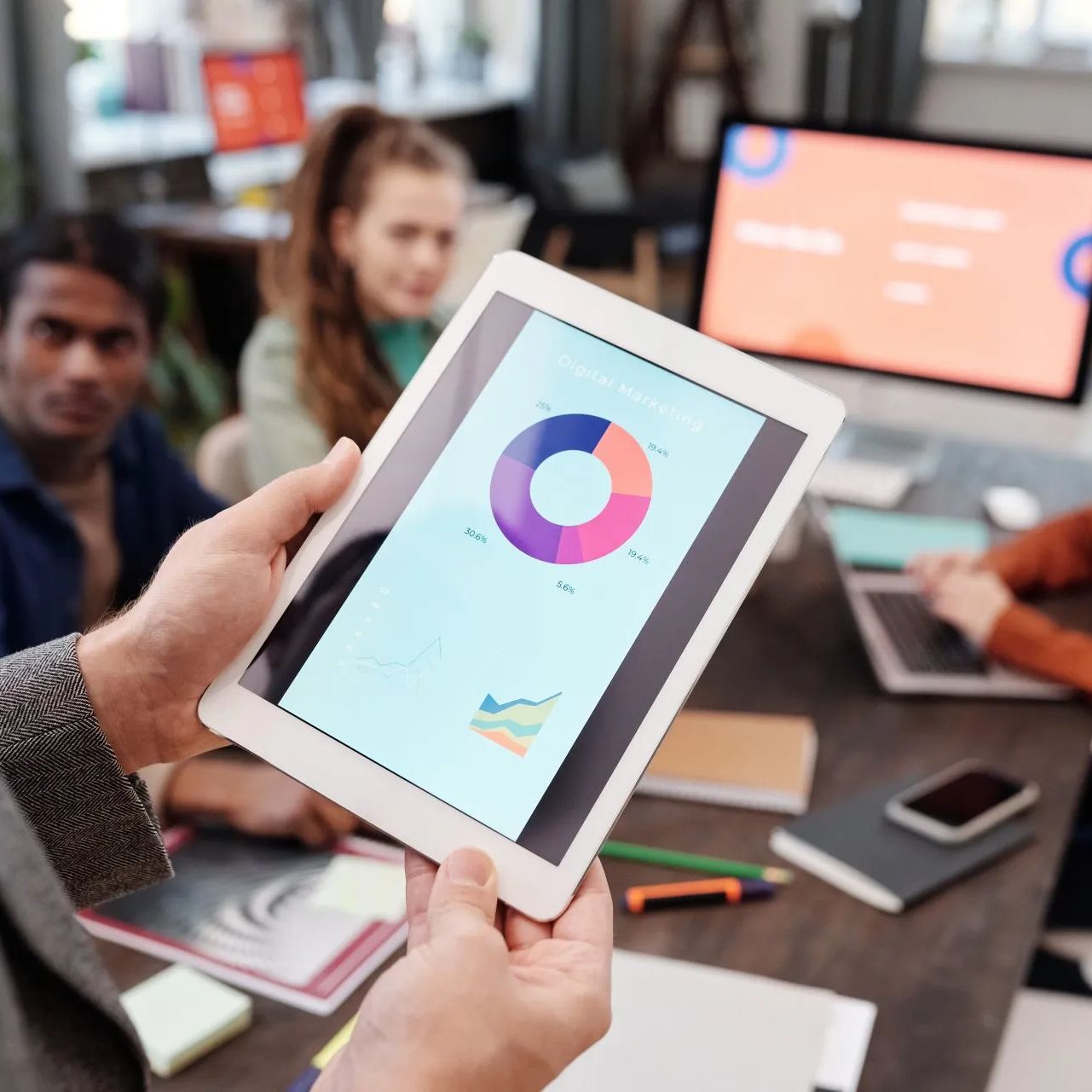 A person is holding a tablet with a pie chart on it.