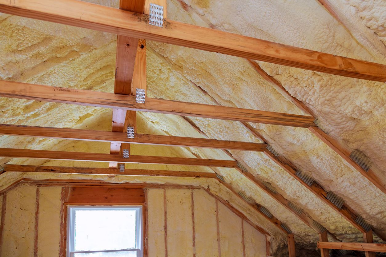The attic of a house is being insulated with spray foam and wooden beams.