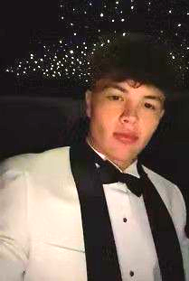 Young person in white tuxedo with black trim, bow tie. Dark background with scattered lights.