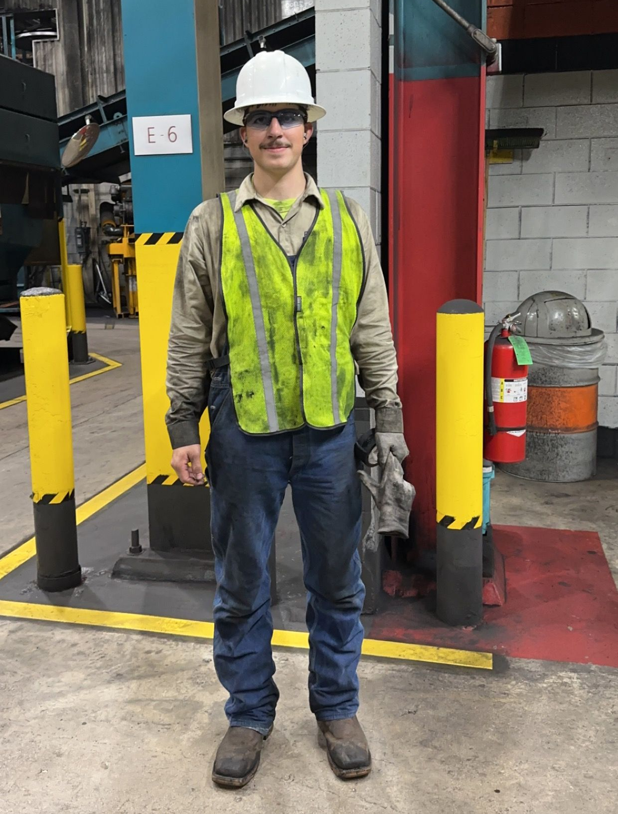 Man in safety vest and hard hat stands in industrial setting.