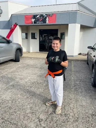 A young boy wearing boxing gloves is standing in front of a building.