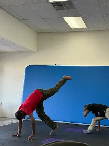 A man in a red shirt is doing a handstand in front of a blue wall