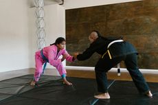 A man and a woman are wrestling on a mat in a gym.