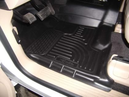 Black floor mat installed in the driver's side footwell of a vehicle with beige interior trim.