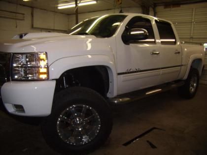 A white pickup truck with a lifted suspension and custom wheels parked inside a garage.