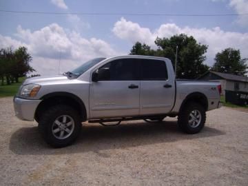 A silver pickup truck parked on a gravel lot under a partly cloudy sky.