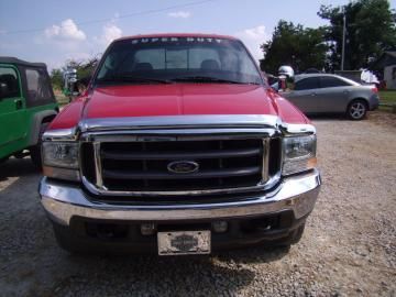 Front view of a red Ford Super Duty truck parked on a gravel lot with other vehicles nearby.