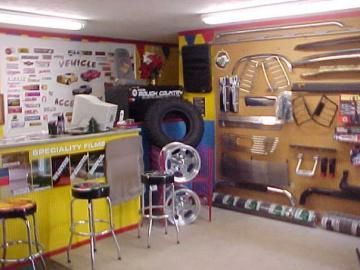 A small vehicle accessory shop with a service counter, stools, and wall-mounted car parts, including wheels and trim.
