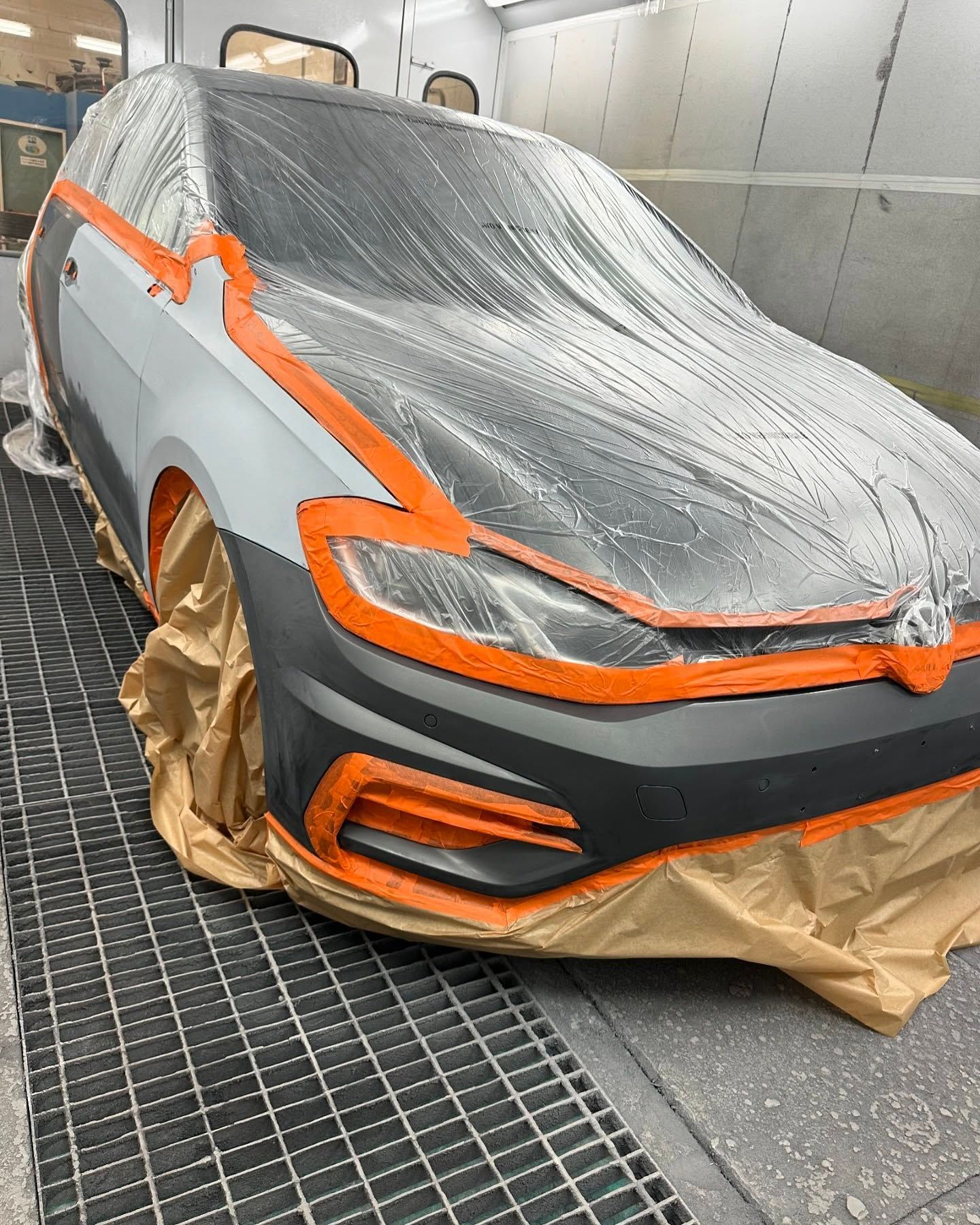 Una Volkswagen Golf grigia parzialmente verniciata, mascherata in preparazione per la verniciatura in una cabina di officina.