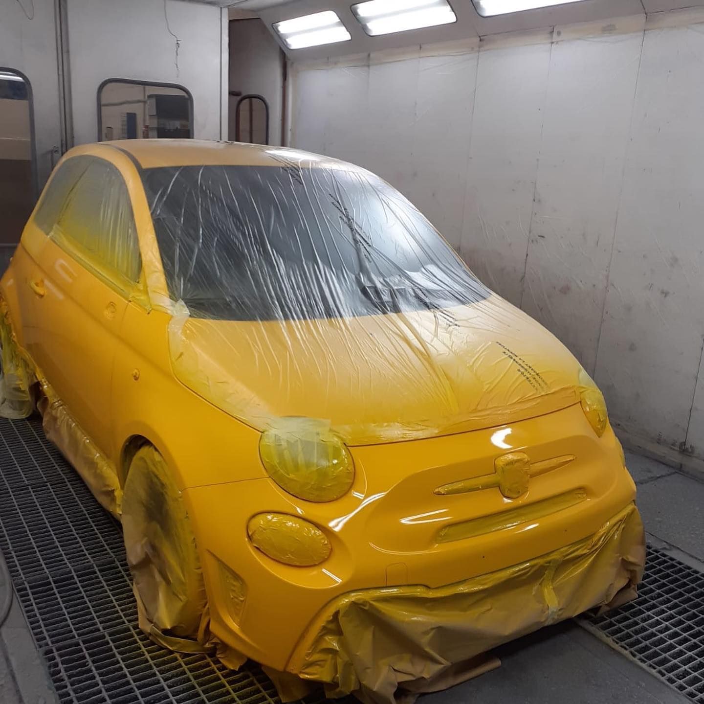 Fiat 500 gialla in una cabina di verniciatura, mascherata per la verniciatura.