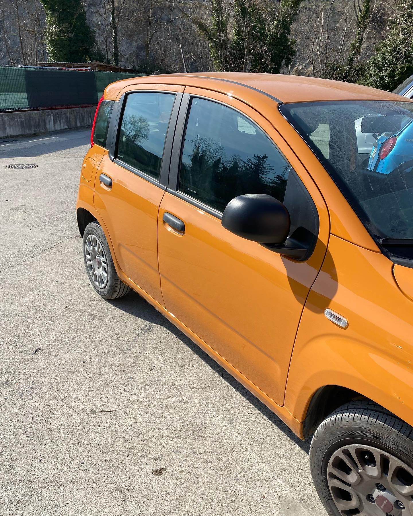 Fiat Panda arancione parcheggiata sull'asfalto. Specchietto laterale nero.