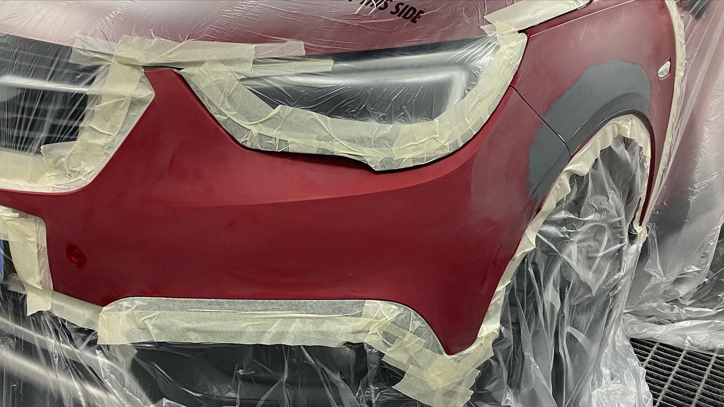 Paraurti di un'auto in preparazione per la verniciatura, nastrato e ricoperto di plastica. Vernice rossa visibile.