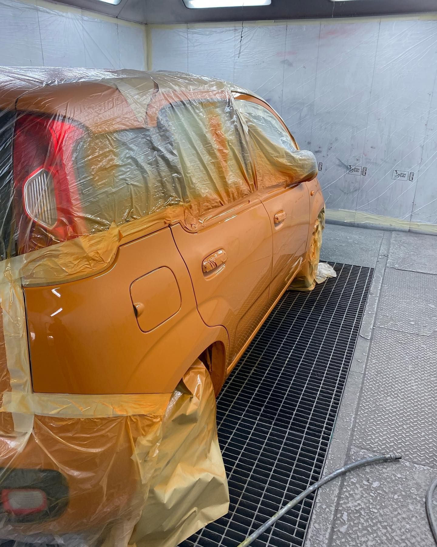 Auto in una cabina di verniciatura, parzialmente mascherata con vernice arancione spruzzata sulla carrozzeria.