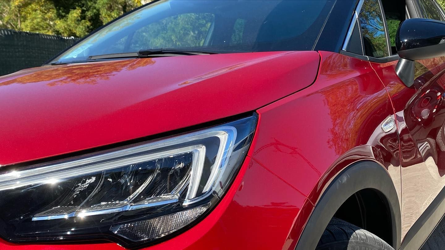 Dettaglio del faro anteriore di un'auto Opel Crossland rossa, parcheggiata all'aperto in una giornata di sole.
