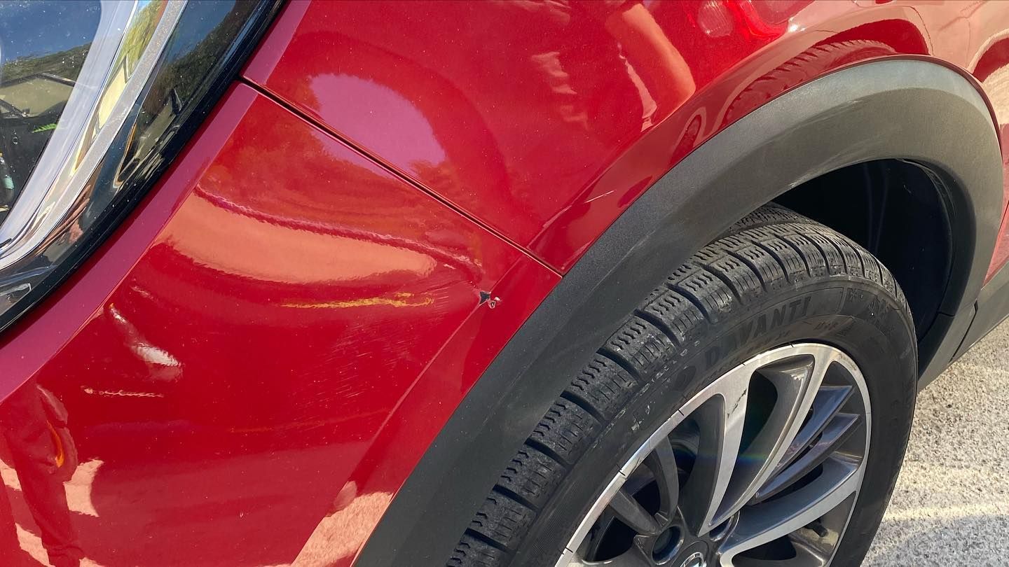 Parafango anteriore di un'auto rossa con un'ammaccatura, accanto a un passaruota e uno pneumatico neri.