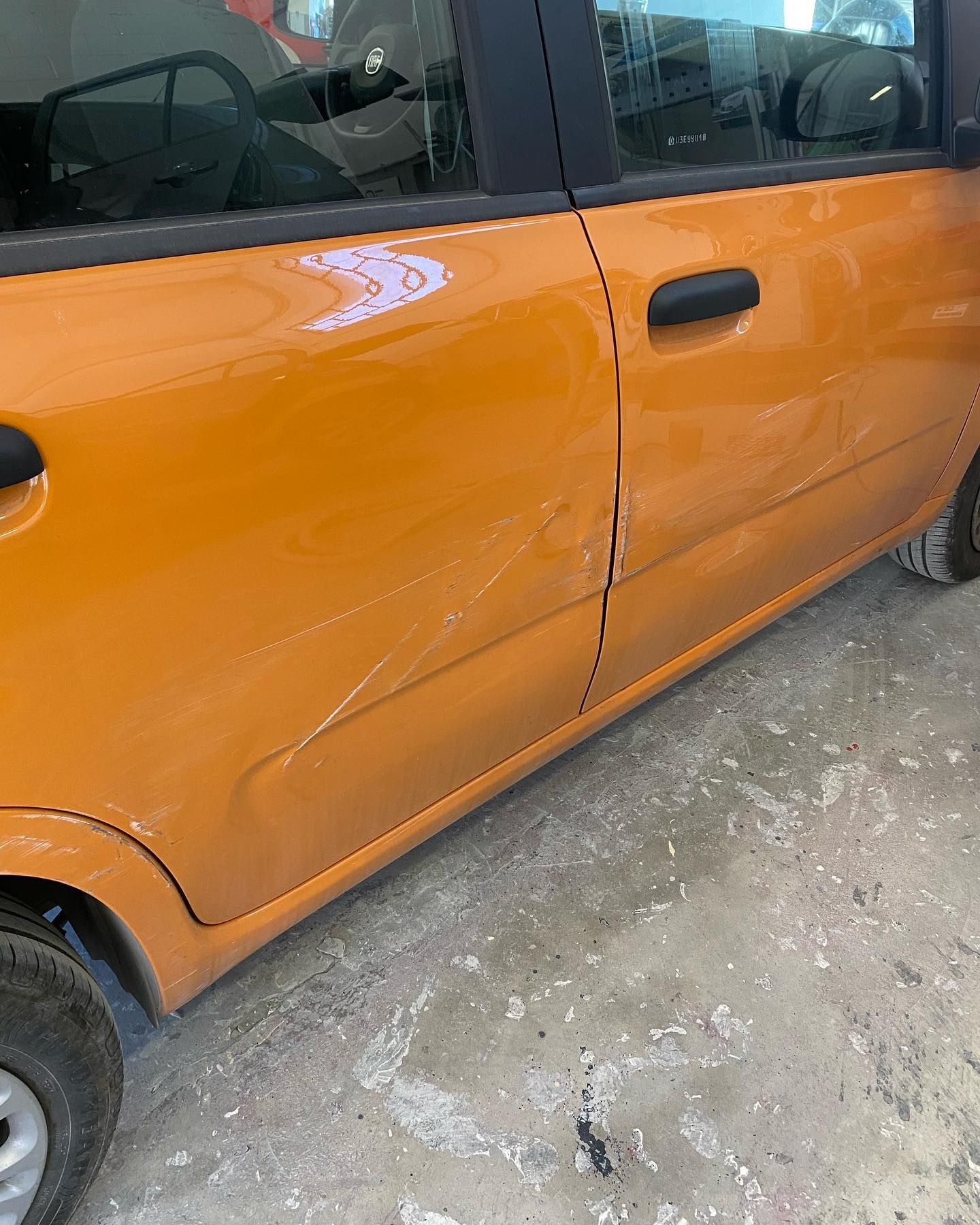 Portiera arancione dell'auto con ammaccature e graffi.