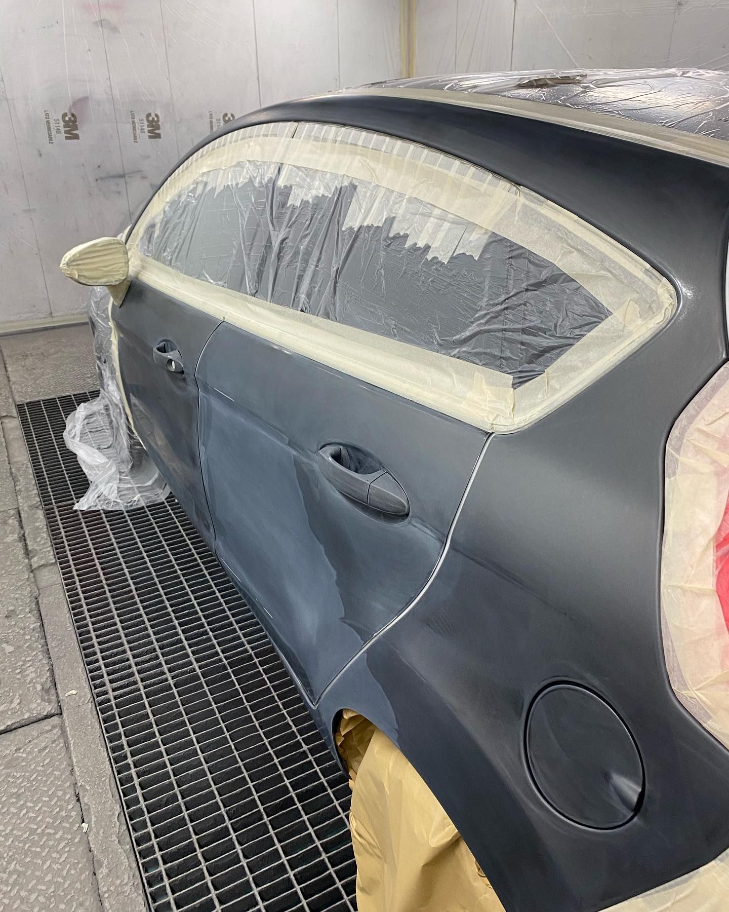 Verniciatura della parte posteriore dell'auto. Applicazione della vernice grigia, mascheratura di finestrini e modanature con nastro adesivo. Carrozzeria in cabina di verniciatura.